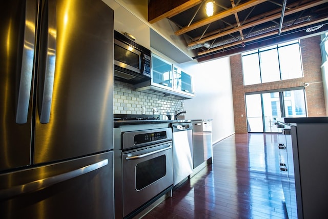 kitchen with decorative backsplash, a towering ceiling, dark hardwood / wood-style flooring, and stainless steel appliances