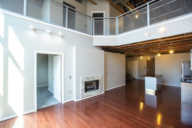 unfurnished living room featuring a fireplace, a towering ceiling, and hardwood / wood-style flooring