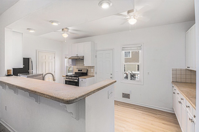 kitchen featuring kitchen peninsula, decorative backsplash, a breakfast bar, stainless steel gas stove, and light hardwood / wood-style floors