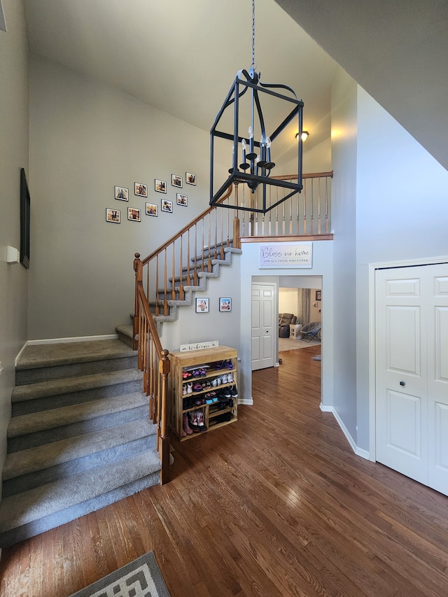 staircase with high vaulted ceiling, wood-type flooring, and an inviting chandelier