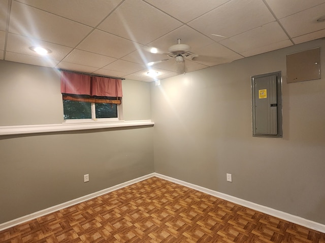 empty room with a drop ceiling, electric panel, parquet floors, and ceiling fan