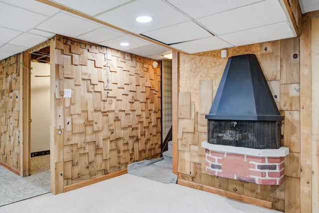 interior space featuring a wood stove, wood walls, and a drop ceiling