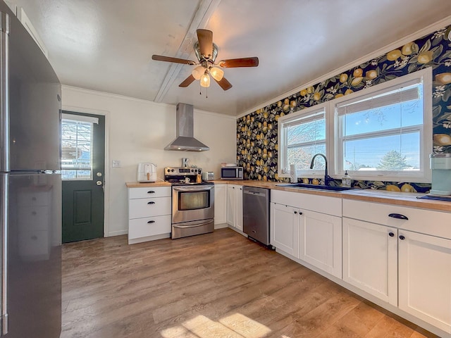 kitchen featuring white cabinetry, sink, stainless steel appliances, wall chimney range hood, and plenty of natural light