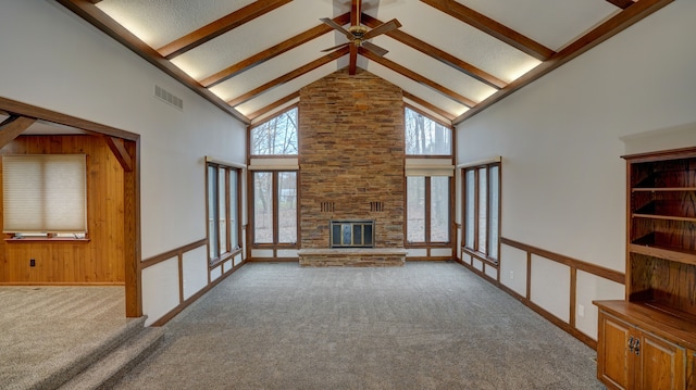 unfurnished living room with wood walls, high vaulted ceiling, a stone fireplace, carpet flooring, and beam ceiling