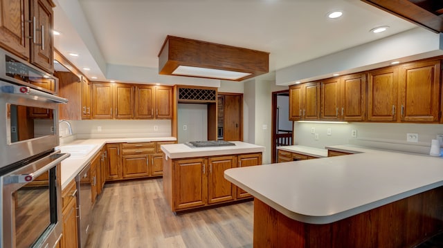 kitchen with a center island, sink, light wood-type flooring, kitchen peninsula, and stainless steel appliances