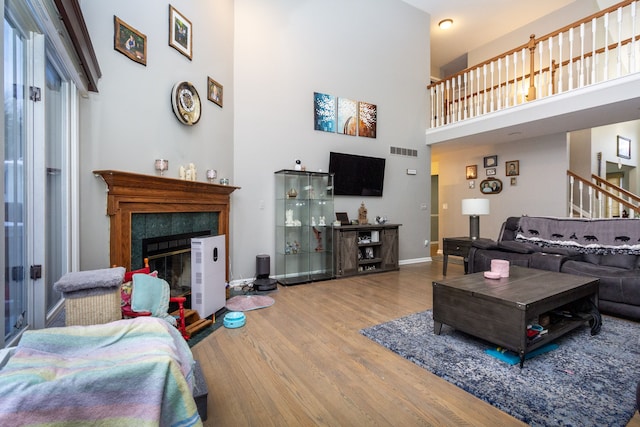 living room with a tiled fireplace, a towering ceiling, and wood-type flooring