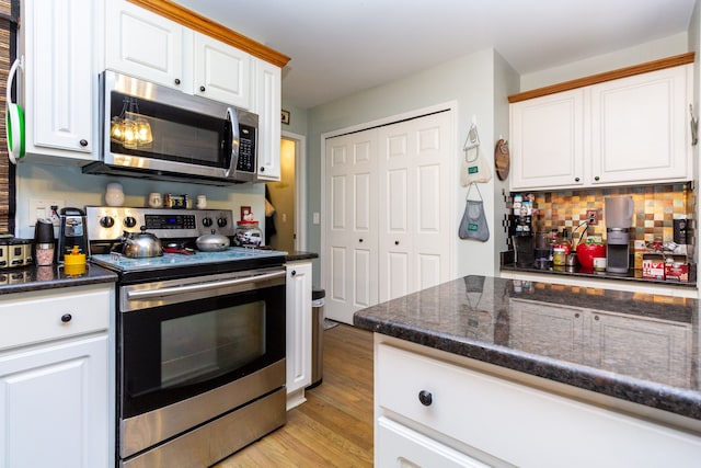 kitchen featuring decorative backsplash, appliances with stainless steel finishes, light wood-type flooring, dark stone countertops, and white cabinets