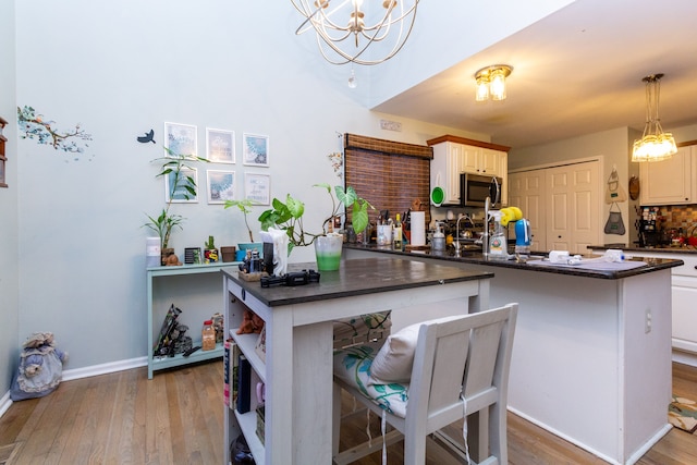 kitchen with kitchen peninsula, white cabinets, hanging light fixtures, and light hardwood / wood-style floors