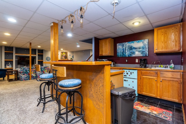 bar featuring sink, a drop ceiling, and dark colored carpet