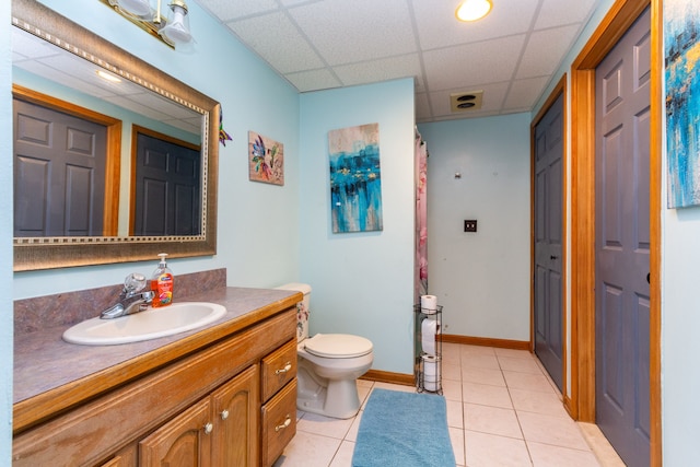 bathroom with toilet, vanity, tile patterned floors, and a drop ceiling