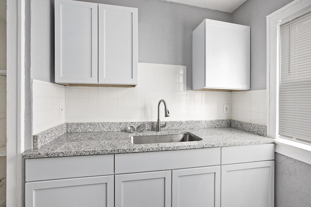 kitchen featuring white cabinets, light stone counters, and sink