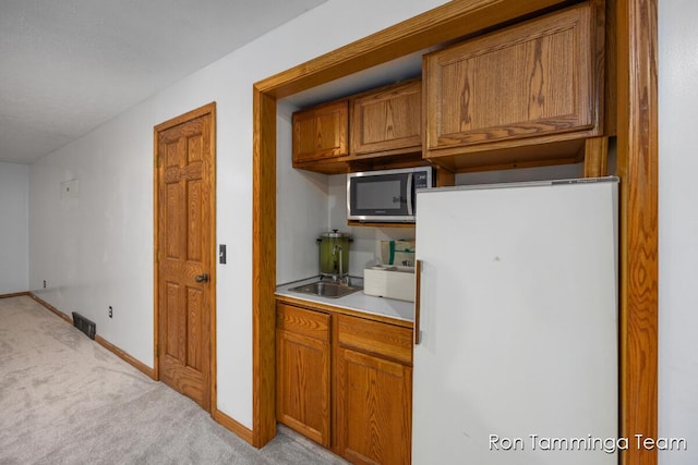 2187 Riley St, Hudsonville, MI 49426 - kitchen with freestanding refrigerator, stainless steel microwave, light colored carpet, brown cabinetry, and baseboards