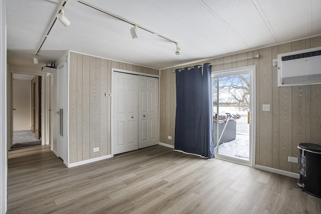 foyer entrance featuring light wood-type flooring, track lighting, a textured ceiling, a wall unit AC, and wooden walls