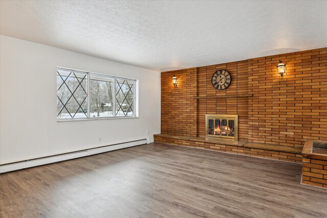 unfurnished living room featuring a baseboard radiator, hardwood / wood-style floors, a textured ceiling, and a brick fireplace