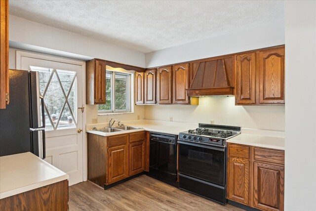 kitchen featuring custom range hood, sink, hardwood / wood-style flooring, a textured ceiling, and black appliances