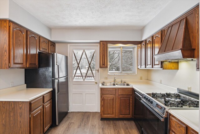 kitchen featuring a textured ceiling, custom range hood, gas range, sink, and light hardwood / wood-style flooring