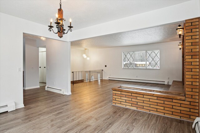 empty room featuring a baseboard radiator, wood-type flooring, and a notable chandelier