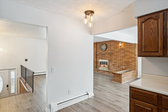 kitchen featuring a brick fireplace, light hardwood / wood-style floors, a textured ceiling, and a baseboard heating unit