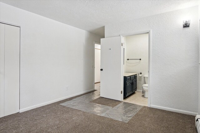 unfurnished bedroom featuring light carpet, baseboard heating, a textured ceiling, and ensuite bathroom