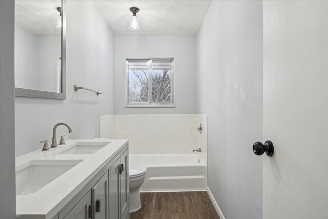 bathroom with a textured ceiling, hardwood / wood-style floors, vanity, toilet, and a bathing tub