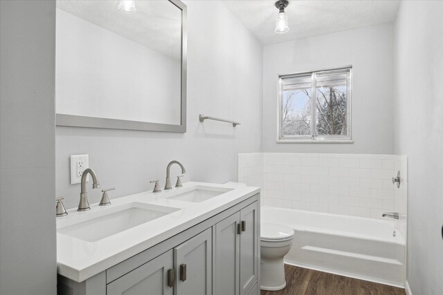 bathroom with toilet, hardwood / wood-style floors, a textured ceiling, a washtub, and vanity