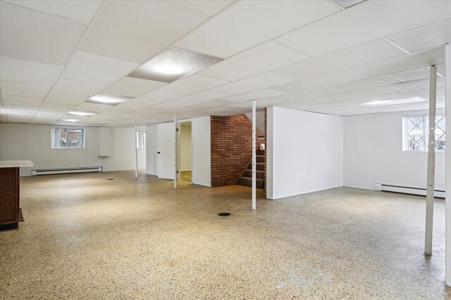 basement featuring brick wall, a paneled ceiling, and baseboard heating