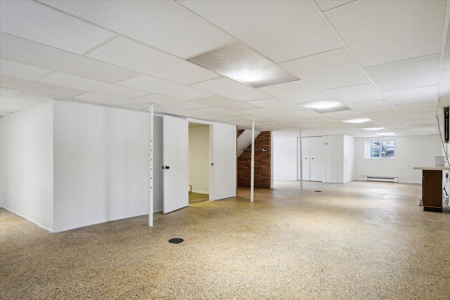 basement with a baseboard radiator and a drop ceiling