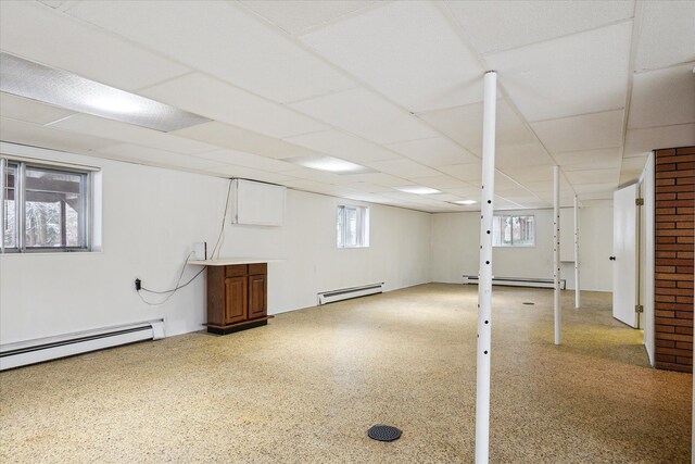 basement featuring baseboard heating, a healthy amount of sunlight, and a paneled ceiling