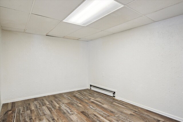 basement with a baseboard radiator, hardwood / wood-style floors, and a drop ceiling