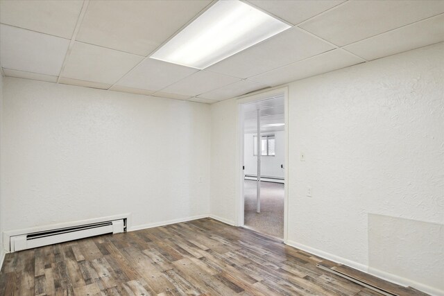 unfurnished room with baseboard heating, a drop ceiling, and hardwood / wood-style floors