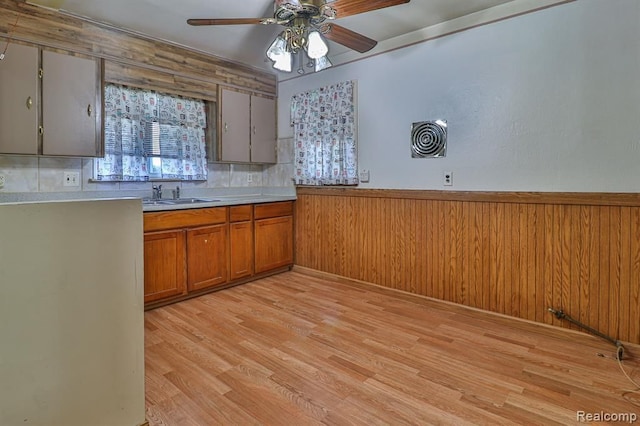 kitchen with light wood-type flooring, ceiling fan, wooden walls, and sink