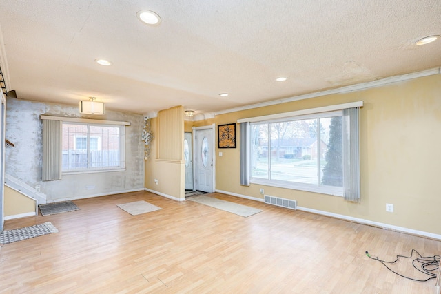 unfurnished living room featuring plenty of natural light, light hardwood / wood-style floors, a textured ceiling, and ornamental molding