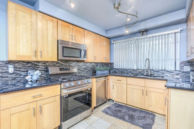 kitchen with appliances with stainless steel finishes, rail lighting, dark stone counters, and sink