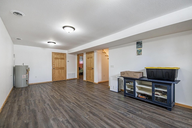 basement with a textured ceiling, dark hardwood / wood-style floors, and water heater