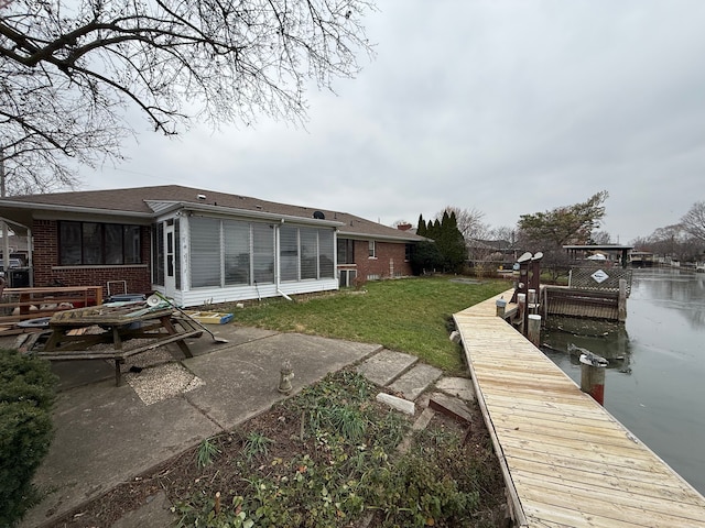 rear view of house featuring a sunroom, brick siding, a yard, and a water view