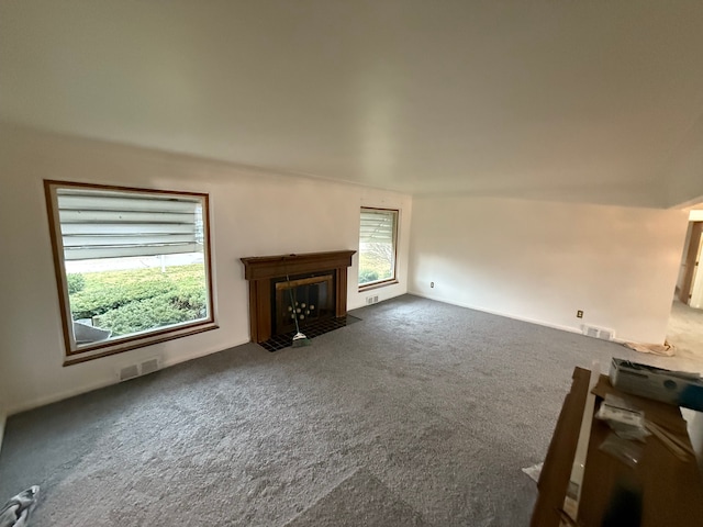 unfurnished living room featuring dark carpet, a fireplace with flush hearth, and visible vents