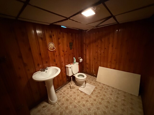 bathroom featuring toilet, a drop ceiling, and wood walls