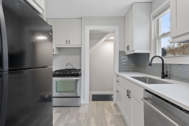 kitchen with white cabinetry, sink, backsplash, appliances with stainless steel finishes, and light wood-type flooring