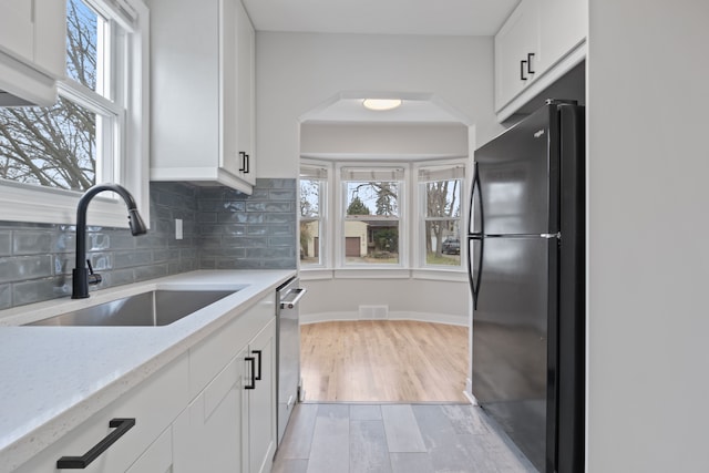 kitchen featuring black refrigerator, white cabinets, a healthy amount of sunlight, and sink