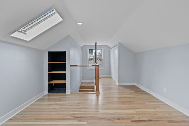 bonus room featuring built in shelves, light hardwood / wood-style flooring, and vaulted ceiling with skylight