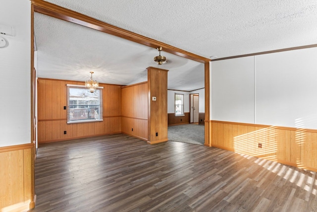 empty room with a chandelier, a textured ceiling, dark hardwood / wood-style floors, and wooden walls