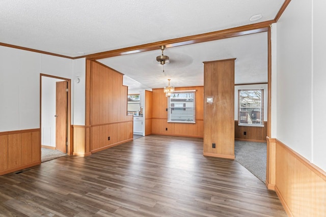 unfurnished living room featuring ornamental molding, ceiling fan with notable chandelier, a textured ceiling, dark wood-type flooring, and wood walls