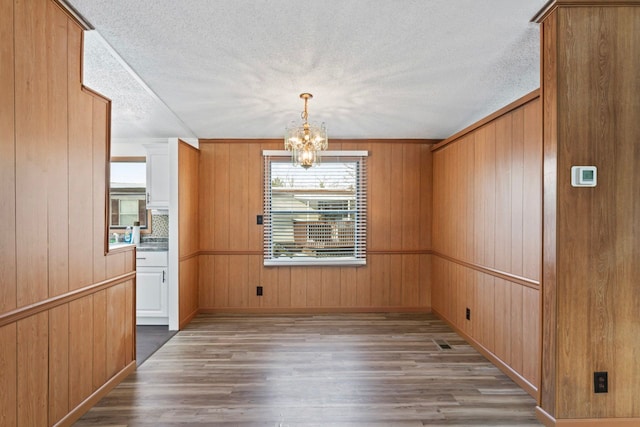 unfurnished dining area featuring dark hardwood / wood-style flooring, a textured ceiling, wooden walls, and an inviting chandelier