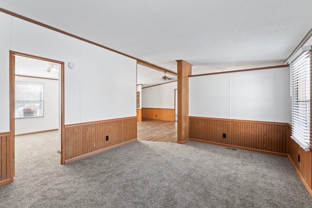 unfurnished room featuring wood walls, light colored carpet, a textured ceiling, and ornamental molding