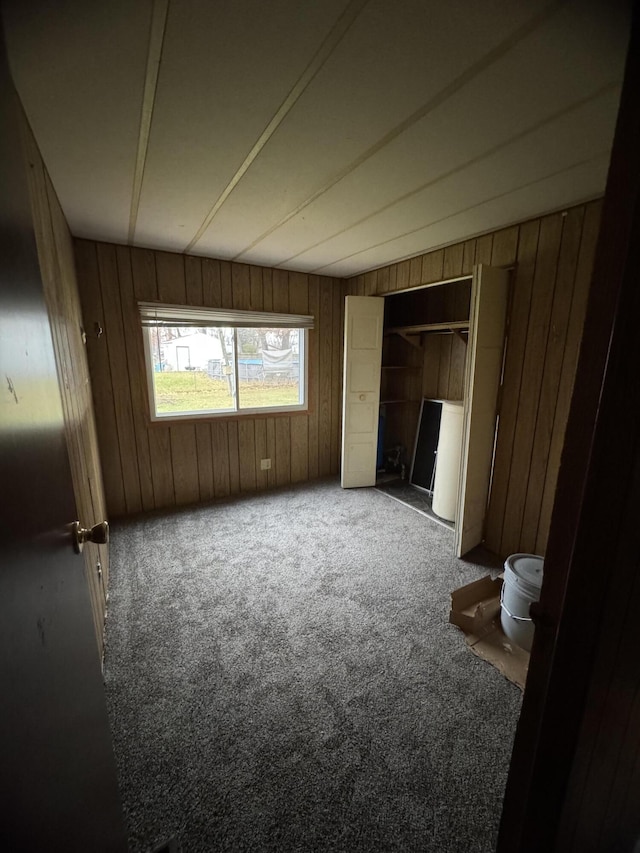 unfurnished bedroom with carpet, wood walls, and a closet