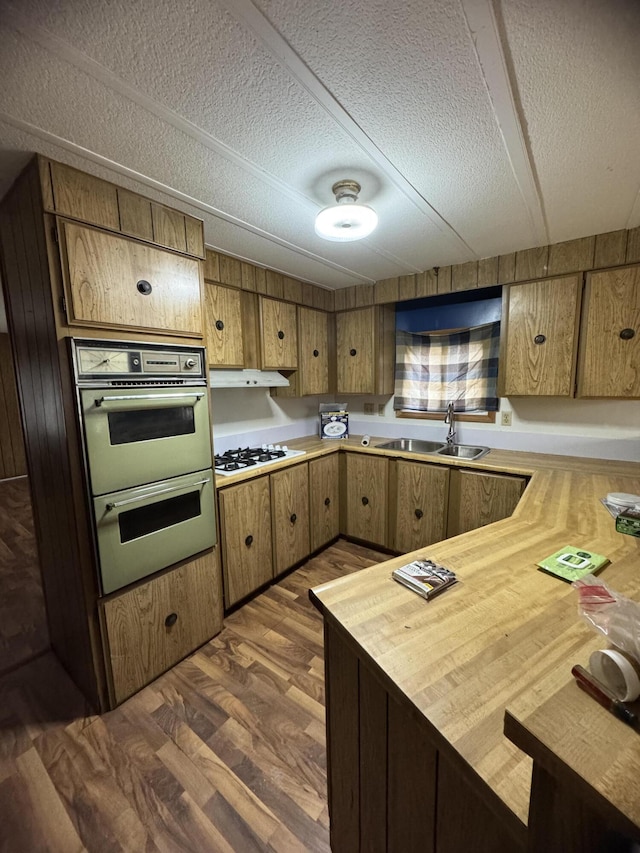 kitchen featuring a textured ceiling, white gas cooktop, double oven, sink, and dark hardwood / wood-style floors