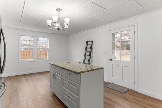 kitchen with light stone countertops, a wealth of natural light, light hardwood / wood-style floors, and hanging light fixtures