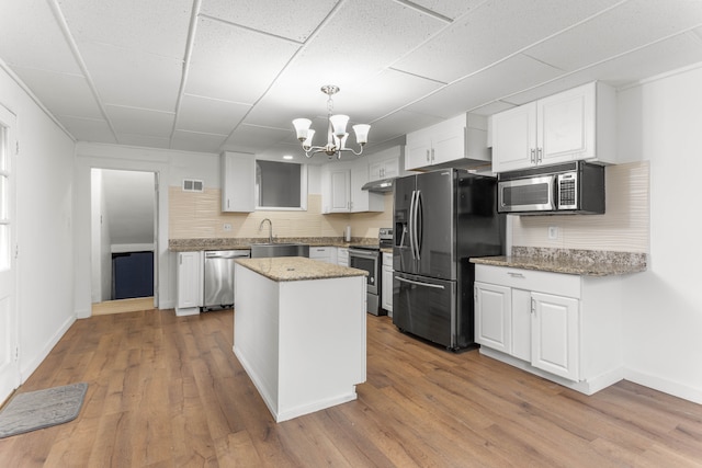 kitchen with appliances with stainless steel finishes, backsplash, white cabinets, light hardwood / wood-style floors, and a kitchen island