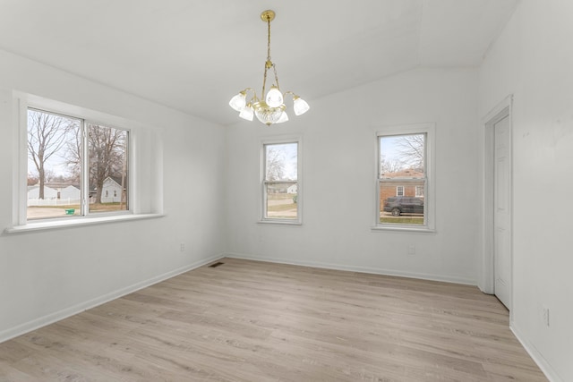 empty room with light hardwood / wood-style flooring, a healthy amount of sunlight, and an inviting chandelier