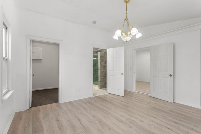 unfurnished bedroom featuring light wood-type flooring, a spacious closet, a closet, and a notable chandelier